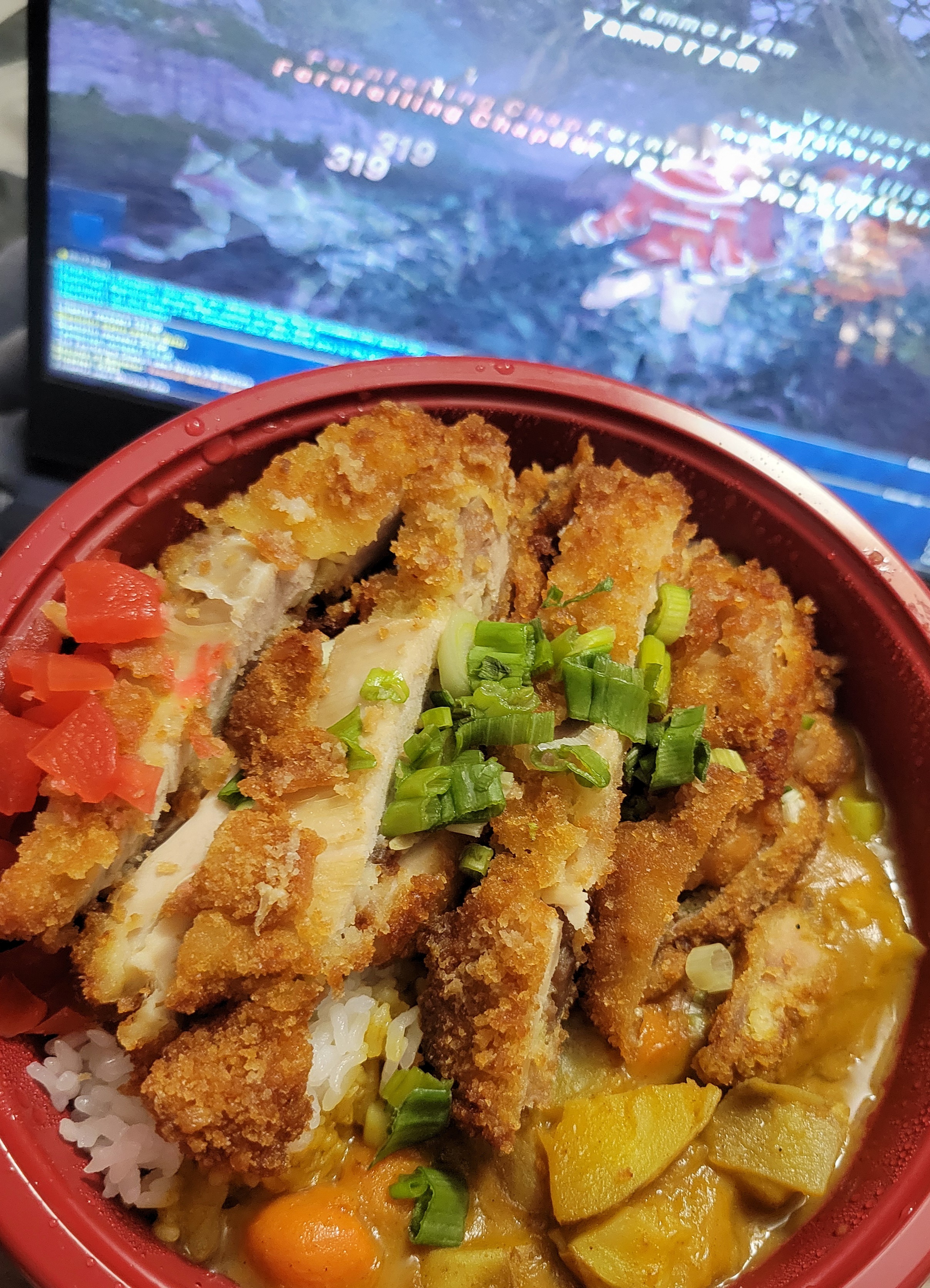 Chicken Japanese curry in a to go bowl with a laptop playing Final Fantasy XI in the background.